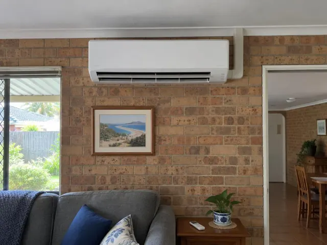 Wall-mounted split system on a brick living room wall above a couch, louvre open, in Helensvale