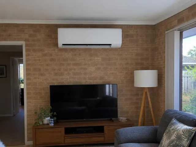 Wall-mounted split system on a brick feature wall above a TV in a living room in Coomera